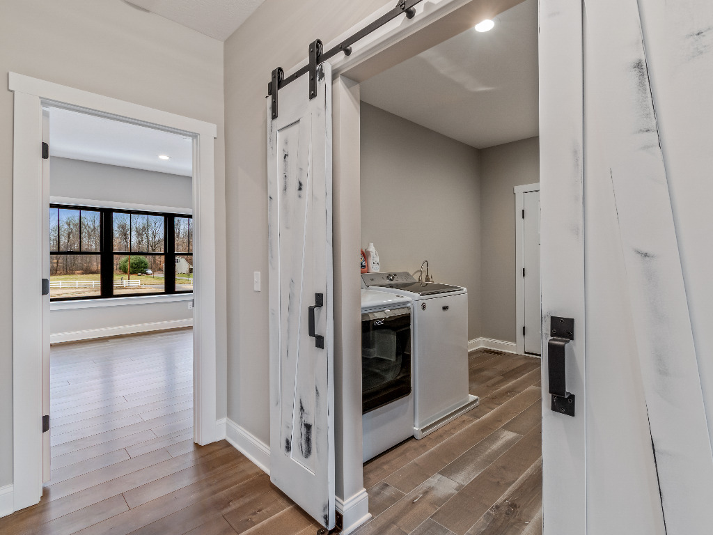 Doorway leading to secondary entryway with laundry machine in Modern Farmhouse Home featuring sliding rustic black and white wooden doors by PH Design, custom construction home builders in Canton, OH
