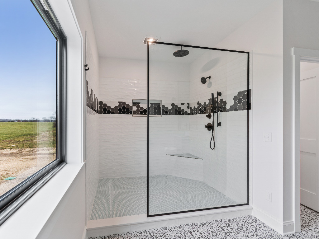 White tile shower with black hexagon niche and glass door next to large window in Modern Farmhouse Home by PH Design, custom construction home builders in Canton, OH
