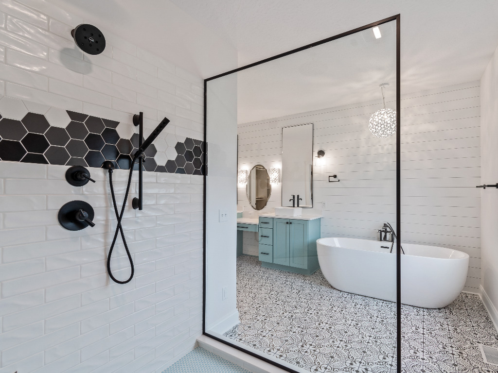 Modern bathroom with white tile shower with black hexagon niche and glass door, white bathtub, and mint green cabinetry in Modern Farmhouse Home by PH Design, custom construction home builders in Canton, OH