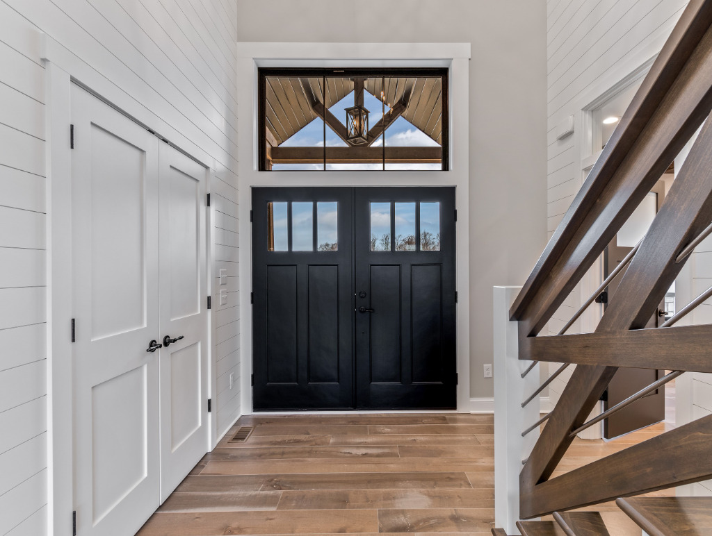 Entryway with large black farmhouse front doors and hardwood flooring by PH Design, custom construction home builders in Canton, OH